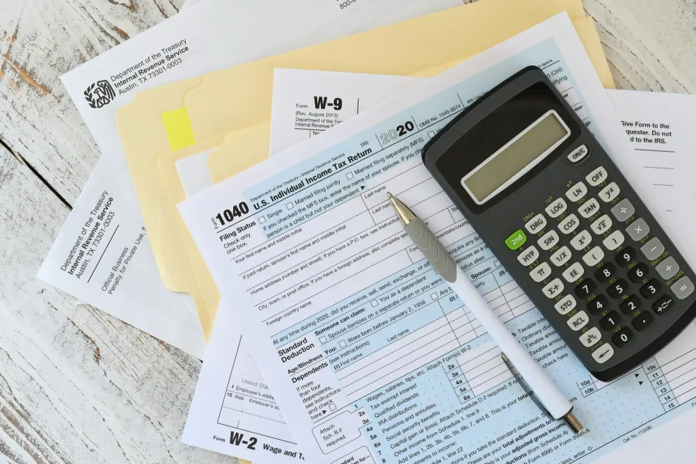 Form 1040, W-9 and W-2 tax documents with a calculator and pen